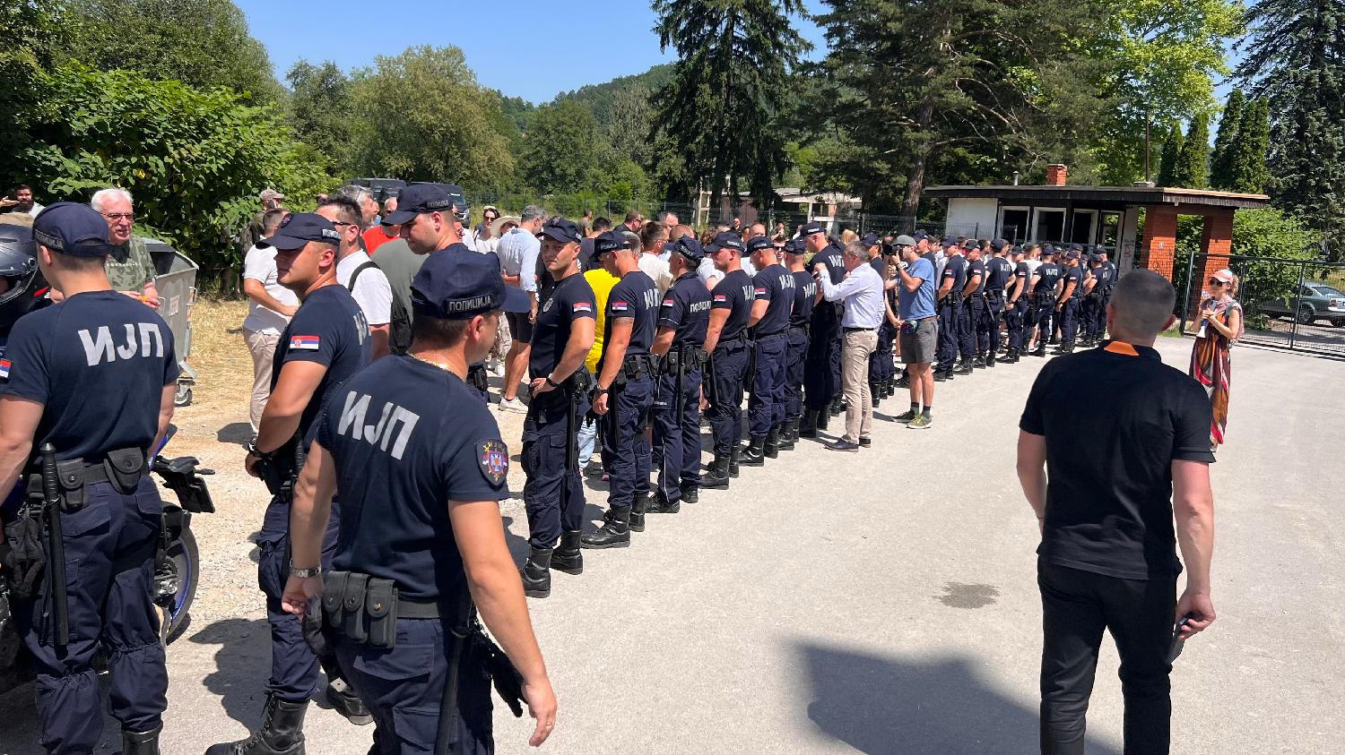 A line of police officers forming a cordon in front of a building in Kosjerić on election day, with citizens gathered behind them.